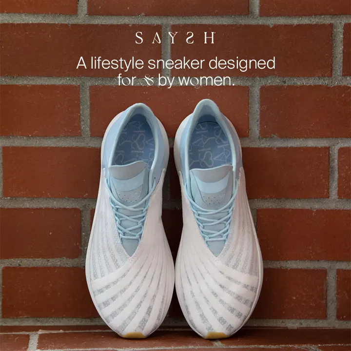 Saysh sneakers against a red brick wall